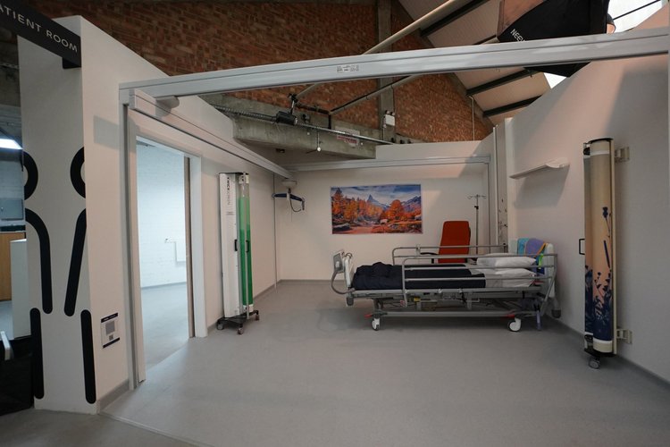 Clinical room with a hospital bed, privacy screen and orange chair.