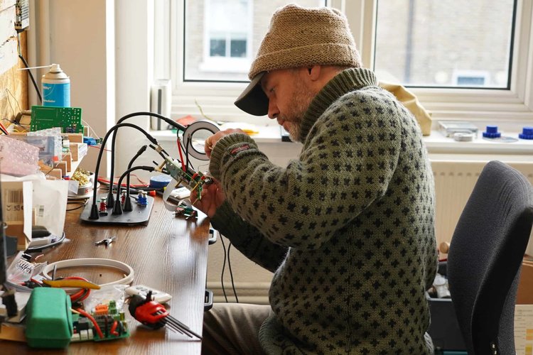 A maker working with small parts at a desk by a window.