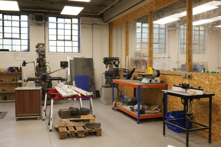 The metal workshop, with machinery, workbenches and tall industrial windows.