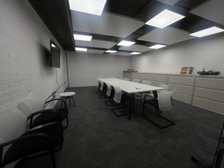 Meeting room with a white table, chairs, cabinets and a wall-mounted screen.