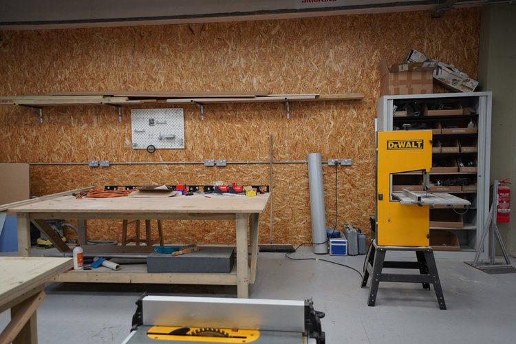 A woodworking workshop with a workbench, power tools, storage shelves, and a DeWalt bandsaw.