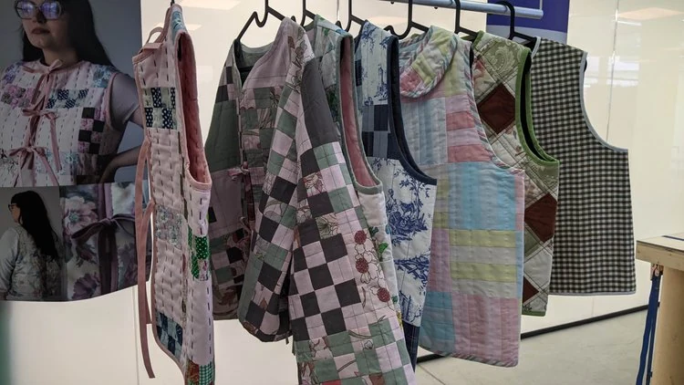 Colorful patchwork quilts and aprons displayed on a rack.