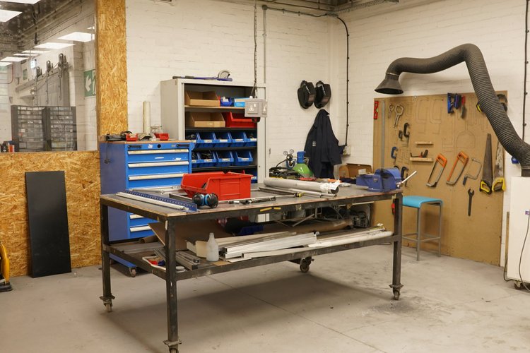 A workshop with a workbench, blue tool drawers, stored tools, and equipment on a pegboard.