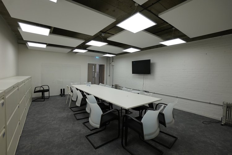 Meeting room with a long white table, chairs and a wall-mounted screen.