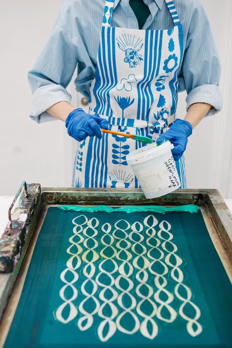 A printmaker adding green ink to a patterned screen.
