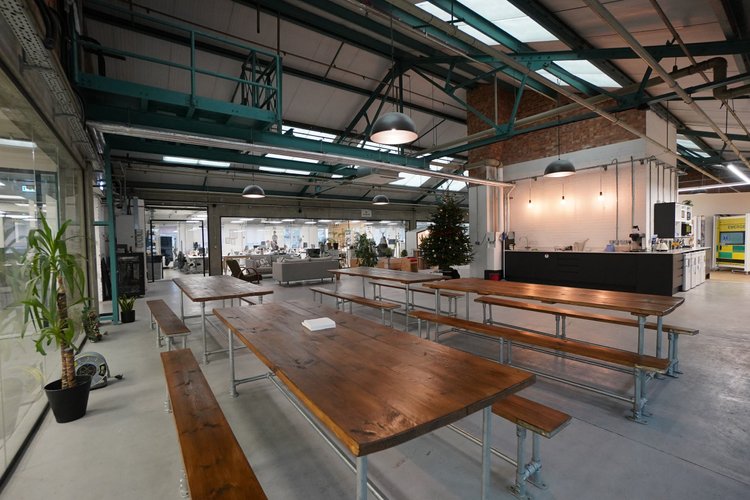 Communal tables beside a kitchen beneath exposed roof beams.