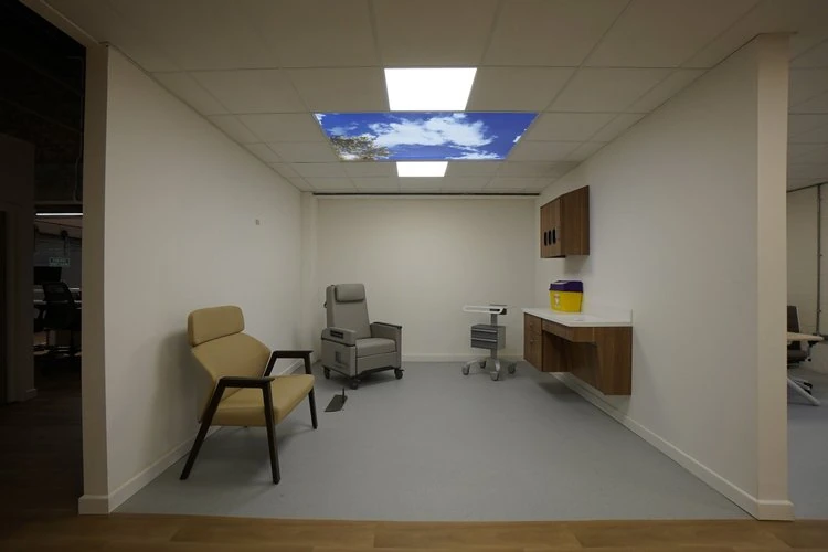Clinical room with patient chairs, a wall cabinet and an illuminated sky ceiling panel.