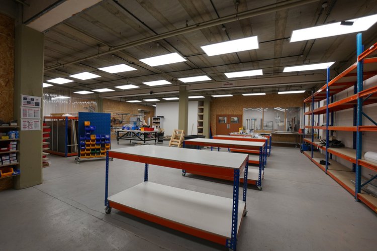 Open workshop with workbenches and orange-and-blue storage racks.