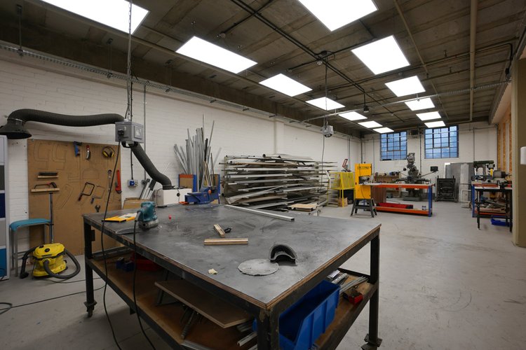 Metalworking workshop with a steel-topped bench, extraction arm and stored metal stock.